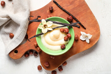 Wall Mural - Wooden board with ramekin of tasty vanilla pudding and hazelnuts on light background, closeup