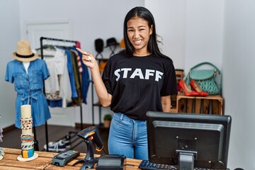 Poster - Young hispanic woman working as staff at retail boutique pointing aside worried and nervous with forefinger, concerned and surprised expression