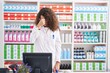 Hispanic woman with curly hair working at pharmacy drugstore tired rubbing nose and eyes feeling fatigue and headache. stress and frustration concept.