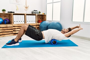 Poster - Young hispanic man doing rehab using foam roller at clinic