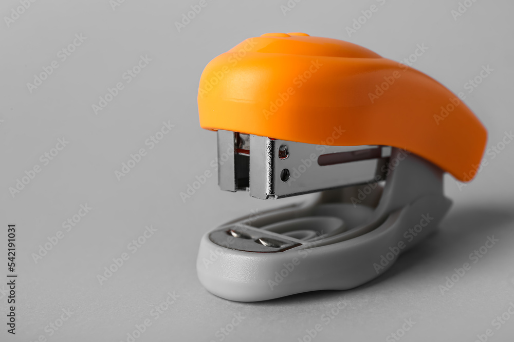 Orange office stapler on grey background