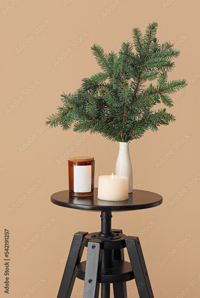 Vase with Christmas branches and burning candle on table near beige wall