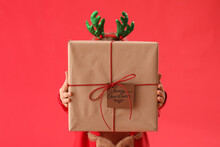 Little Girl In Reindeer Horns With Christmas Gift On Red Background, Closeup