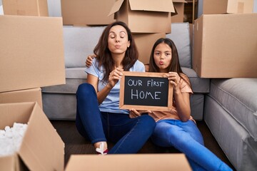 Canvas Print - Young mother and daughter sitting on the floor at new home puffing cheeks with funny face. mouth inflated with air, catching air.