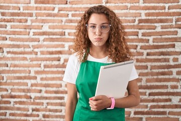 Sticker - Young caucasian woman holding art notebook puffing cheeks with funny face. mouth inflated with air, crazy expression.