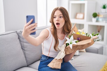 Poster - Caucasian woman holding bouquet of white flowers taking a selfie picture afraid and shocked with surprise and amazed expression, fear and excited face.