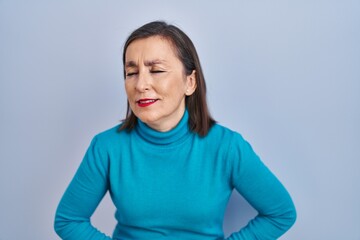 Wall Mural - Middle age hispanic woman standing over isolated background with hand on stomach because indigestion, painful illness feeling unwell. ache concept.