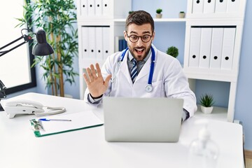 Poster - Young hispanic man wearing doctor uniform having video call at clinic