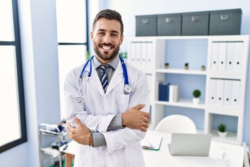 Sticker - Handsome hispanic man wearing doctor uniform and stethoscope at medical clinic happy face smiling with crossed arms looking at the camera. positive person.