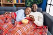 © Krakenimages.com - Young african american couple sitting on the sofa watching tv smiling and laughing hard out loud because funny crazy joke.
