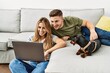 © Krakenimages.com - Young hispanic couple smiling happy using laptop sitting on the sofa  with dog at home.