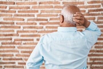 Sticker - Senior man with grey hair standing over bricks wall backwards thinking about doubt with hand on head