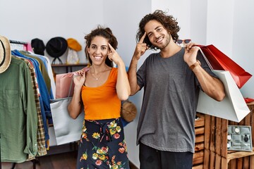 Wall Mural - Young hispanic couple holding shopping bags at retail shop smiling pointing to head with one finger, great idea or thought, good memory