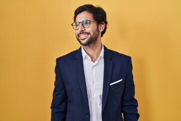 Poster - Handsome latin man standing over yellow background looking away to side with smile on face, natural expression. laughing confident.