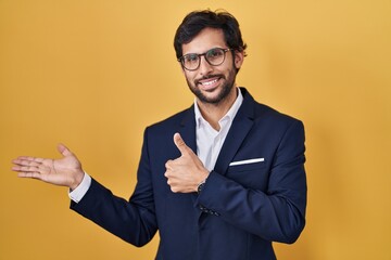 Sticker - Handsome latin man standing over yellow background showing palm hand and doing ok gesture with thumbs up, smiling happy and cheerful