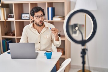 Poster - Handsome latin man recording bitcoin tutorial with smartphone at home scared and amazed with open mouth for surprise, disbelief face