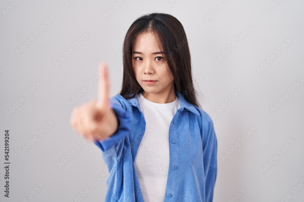 Young chinese woman standing over white background pointing with finger ...