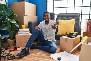 Poster - African american man sitting on the floor at new home smiling friendly offering handshake as greeting and welcoming. successful business.