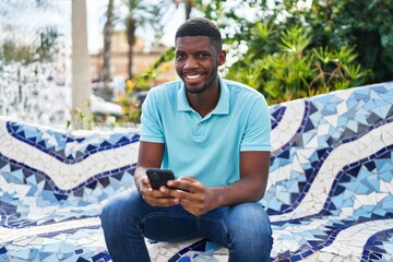 Wall Mural - Young african american man smiling confident using smartphone at park