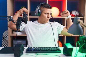 Poster - Young hispanic man playing video games showing arms muscles smiling proud. fitness concept.