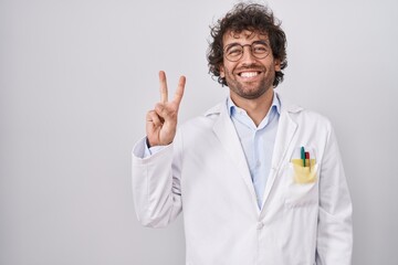 Sticker - Hispanic young man wearing doctor uniform showing and pointing up with fingers number two while smiling confident and happy.