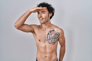 Wall Mural - Hispanic man standing shirtless very happy and smiling looking far away with hand over head. searching concept.