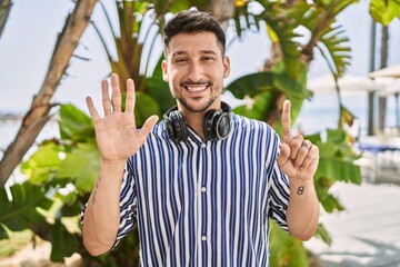 Poster - Young handsome man listening to music using headphones outdoors showing and pointing up with fingers number six while smiling confident and happy.