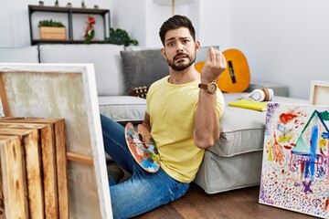 Young man with beard painting canvas at home doing italian gesture with hand and fingers confident expression