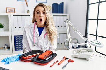 Sticker - Young beautiful doctor woman with reflex hammer and medical instruments afraid and shocked with surprise expression, fear and excited face.