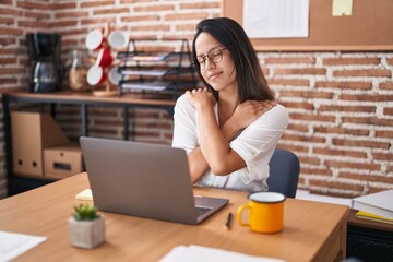 Wall Mural - Hispanic young woman working at the office wearing glasses hugging oneself happy and positive, smiling confident. self love and self care