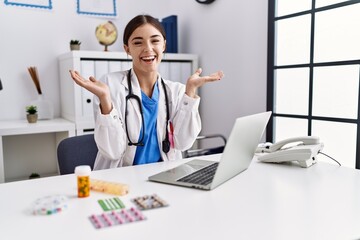 Poster - Young hispanic doctor woman wearing doctor uniform working at the clinic celebrating mad and crazy for success with arms raised and closed eyes screaming excited. winner concept