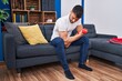 © Krakenimages.com - Young hispanic man training using dumbbell sitting on sofa at home