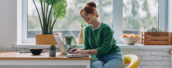 Beautiful young woman working on laptop while sitting at the table at home