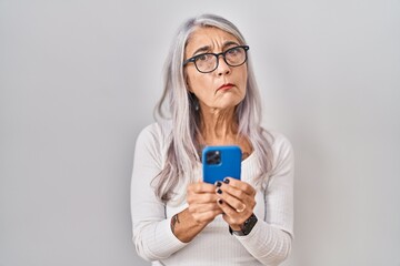 Sticker - Middle age woman with grey hair using smartphone typing message clueless and confused expression. doubt concept.