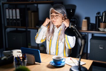 Sticker - Middle age woman with grey hair working at the office at night covering ears with fingers with annoyed expression for the noise of loud music. deaf concept.