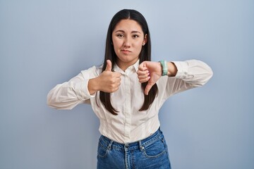 Sticker - Young latin woman standing over blue background doing thumbs up and down, disagreement and agreement expression. crazy conflict