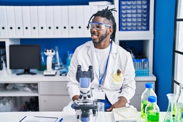 Poster - African man with dreadlocks working at scientist laboratory looking to side, relax profile pose with natural face and confident smile.