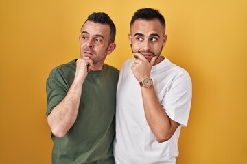 Poster - Homosexual couple standing over yellow background thinking worried about a question, concerned and nervous with hand on chin