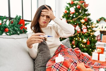 Poster - Middle age hispanic woman using thermometer sitting by christmas tree at home