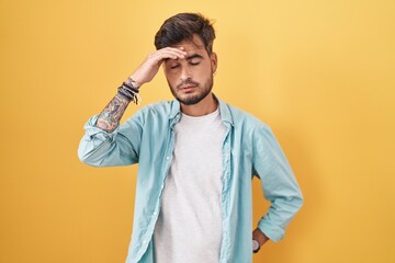 Sticker - Young hispanic man with tattoos standing over yellow background worried and stressed about a problem with hand on forehead, nervous and anxious for crisis