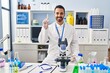 © Krakenimages.com - Young hispanic man with beard working at scientist laboratory showing and pointing up with finger number one while smiling confident and happy.