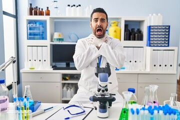 Poster - Young hispanic man with beard working at scientist laboratory shouting and suffocate because painful strangle. health problem. asphyxiate and suicide concept.