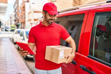 Sticker - Young hispanic man courier using touchpad holding package at street