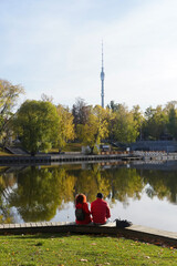 Couple in red cloths sitting on the river bank in the autumn park