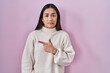 Young south asian woman standing over pink background pointing aside worried and nervous with forefinger, concerned and surprised expression