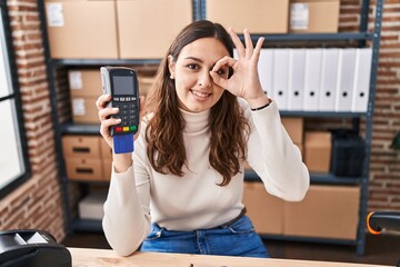 Sticker - Young hispanic woman working at small business ecommerce holding dataphone smiling happy doing ok sign with hand on eye looking through fingers