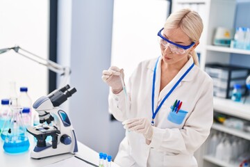 Poster - Young blonde woman wearing scientist uniform measuring liquid at laboratory