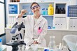 © Krakenimages.com - Hispanic girl with down syndrome working at scientist laboratory smiling and confident gesturing with hand doing small size sign with fingers looking and the camera. measure concept.
