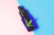 Eyedropper bottle with Cannabis CBD oil and Marijuana leaf on Pink Blue background