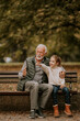 © BGStock72 - Grandfather spending time with his granddaughter on bench in park on autumn day
